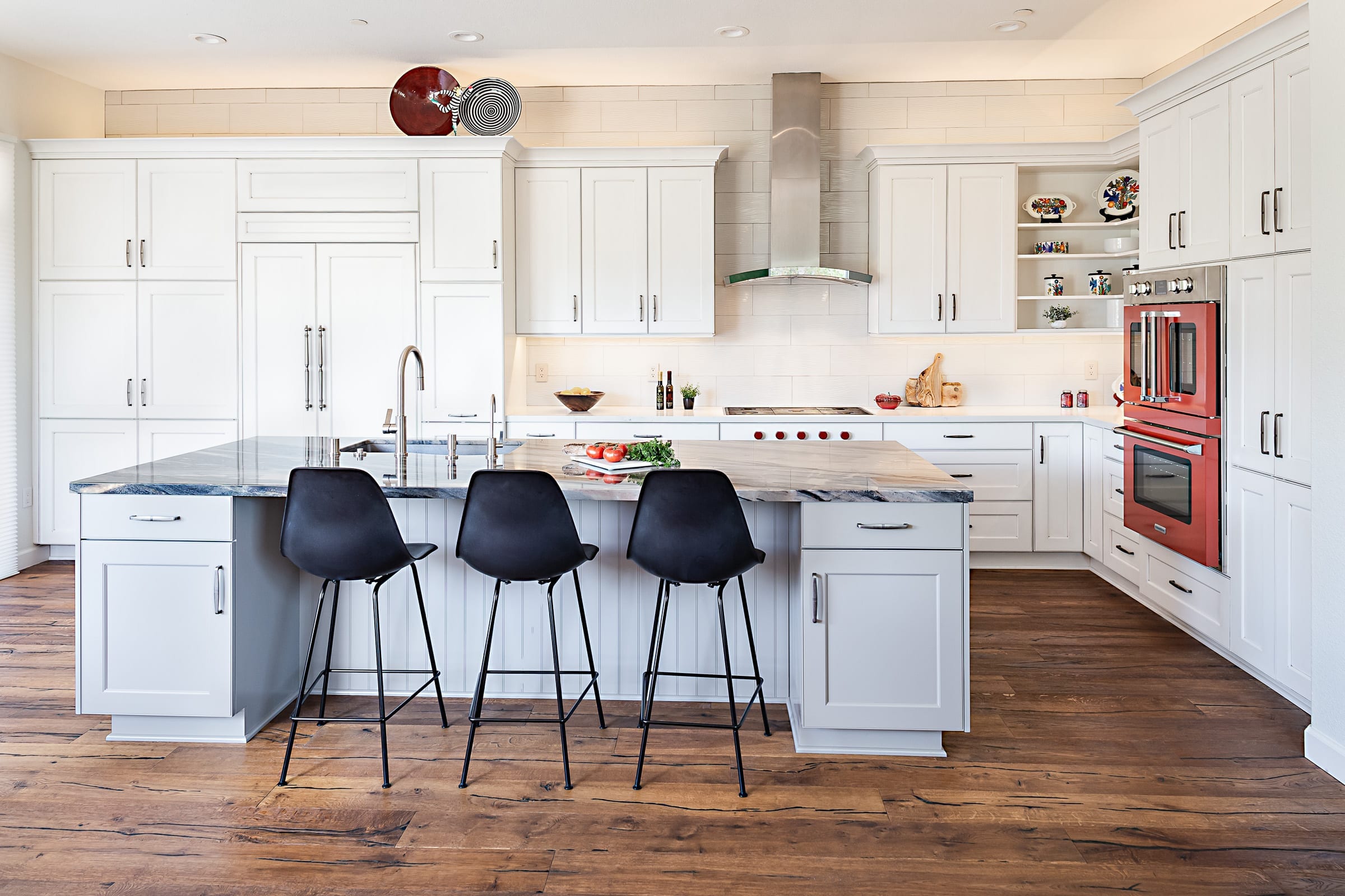 Large kitchen with white and grey cabinets and large island with black seating for 3 in bar height chairs