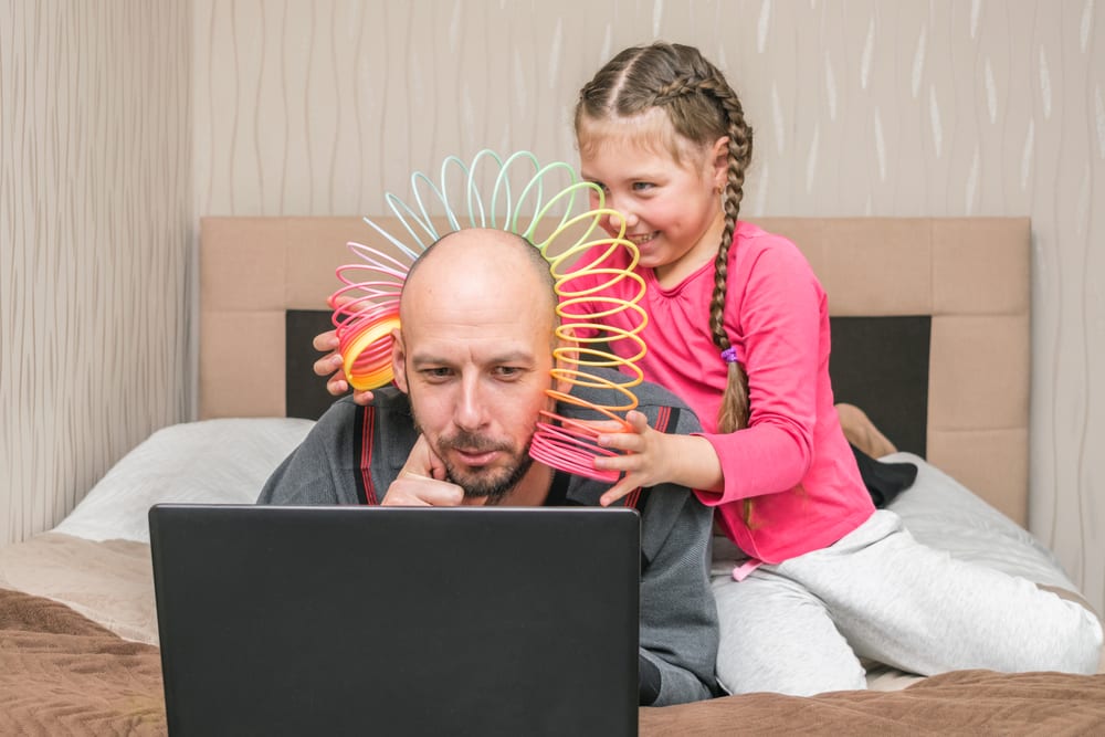 father with kid playing on him while trying to work in bedroom