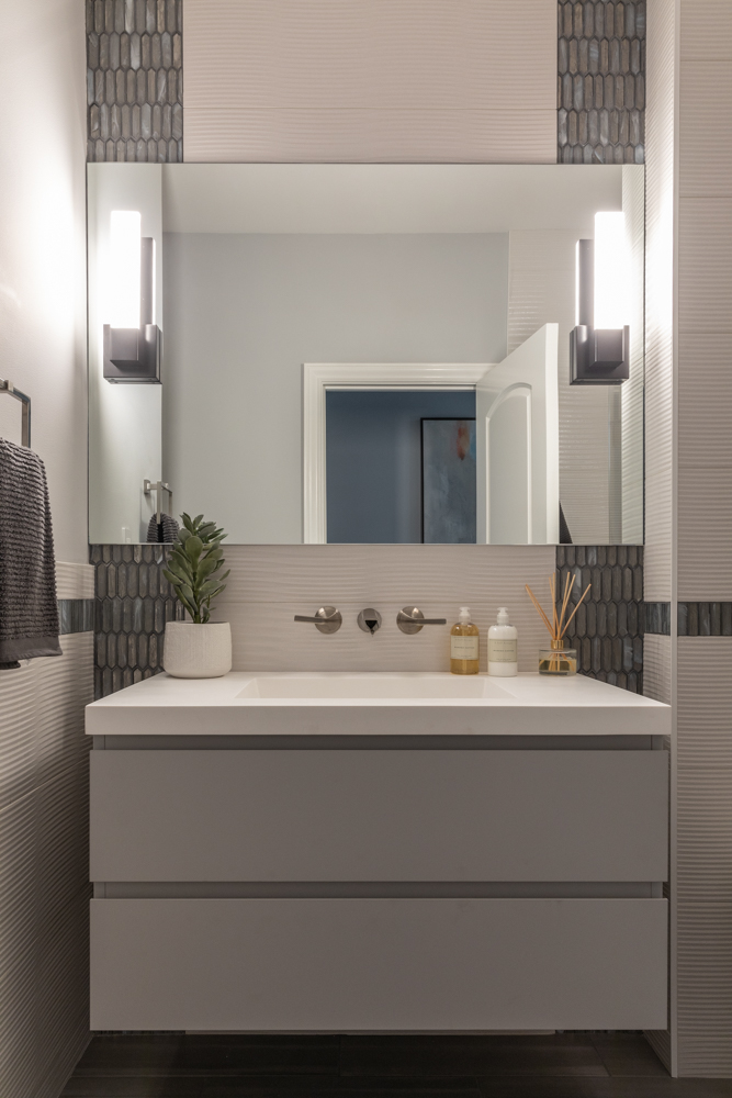Hall bath with vertical tile, mirror mounted sconces, floating vanity