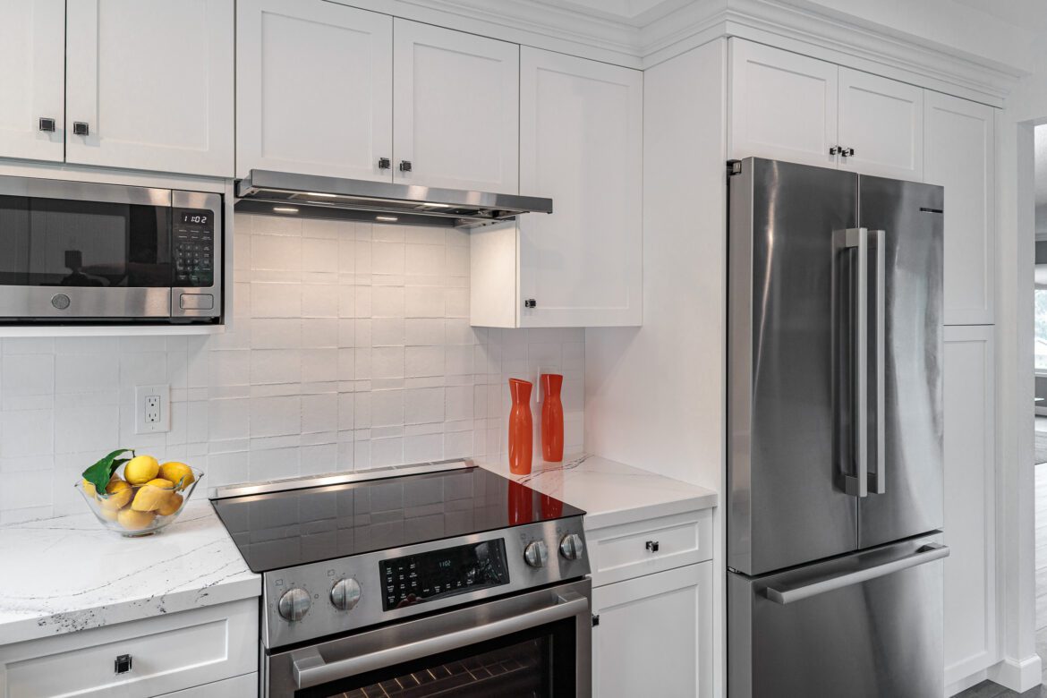 White cabinets, stainless steel appliances, textured matte white tile backsplash, slimline hood