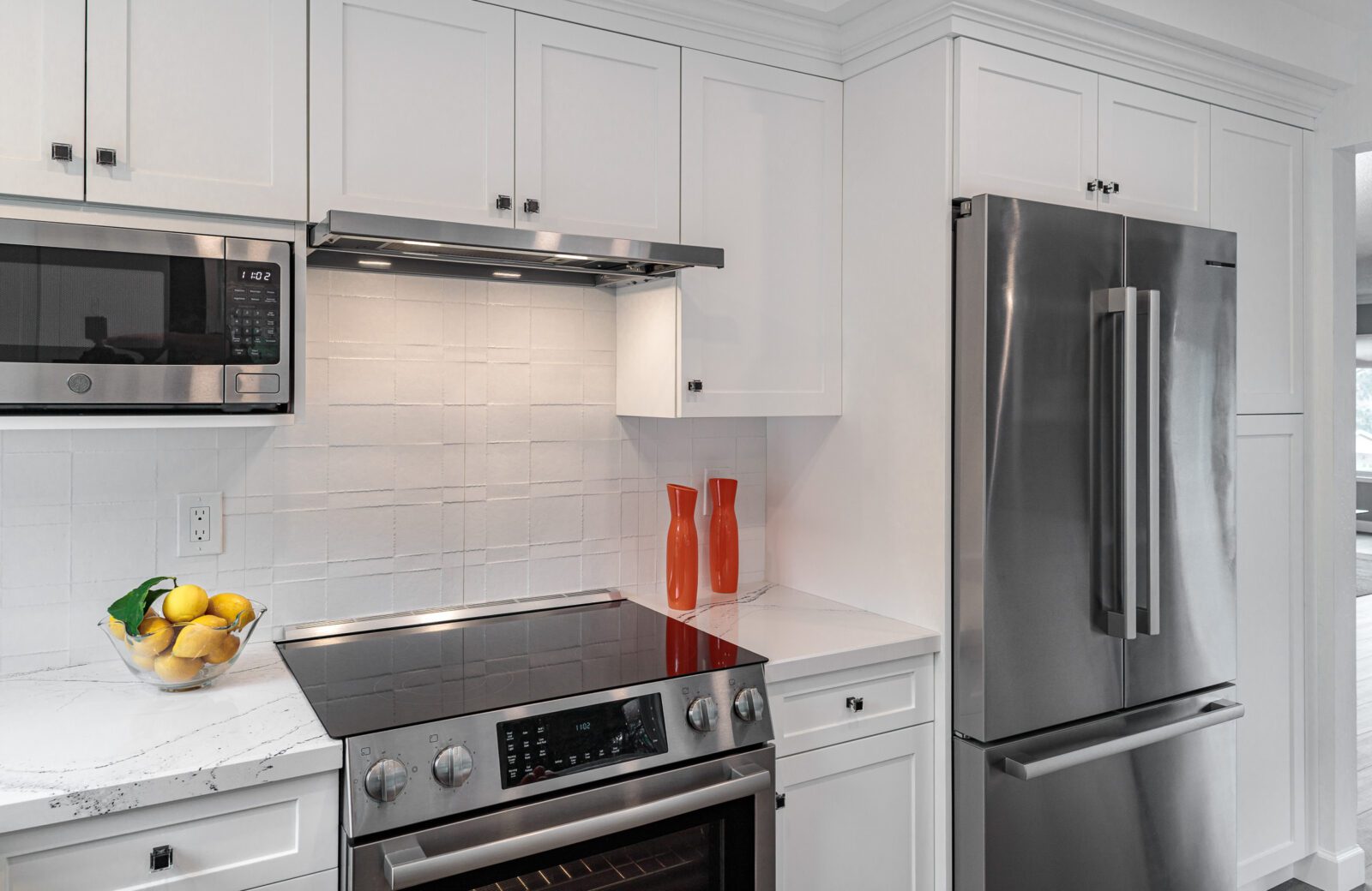 White cabinets, stainless steel appliances, textured matte white tile backsplash, slimline hood