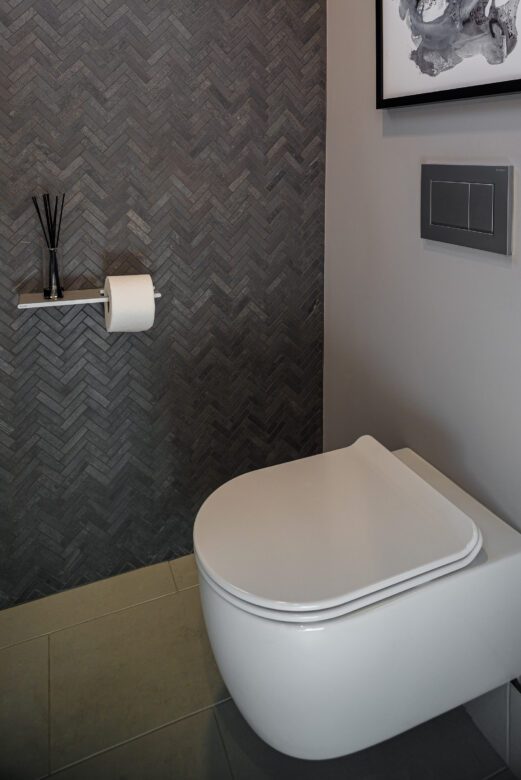 Water closet with dark grey chevron tile wall, white tankless wall mounted toilet
