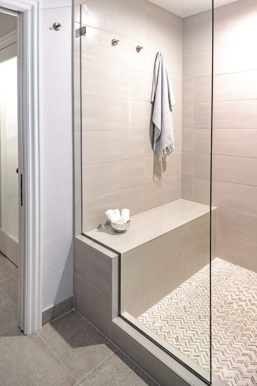 large white and beige shower with tile bench, towel hooks in shower, small chevron tile floor