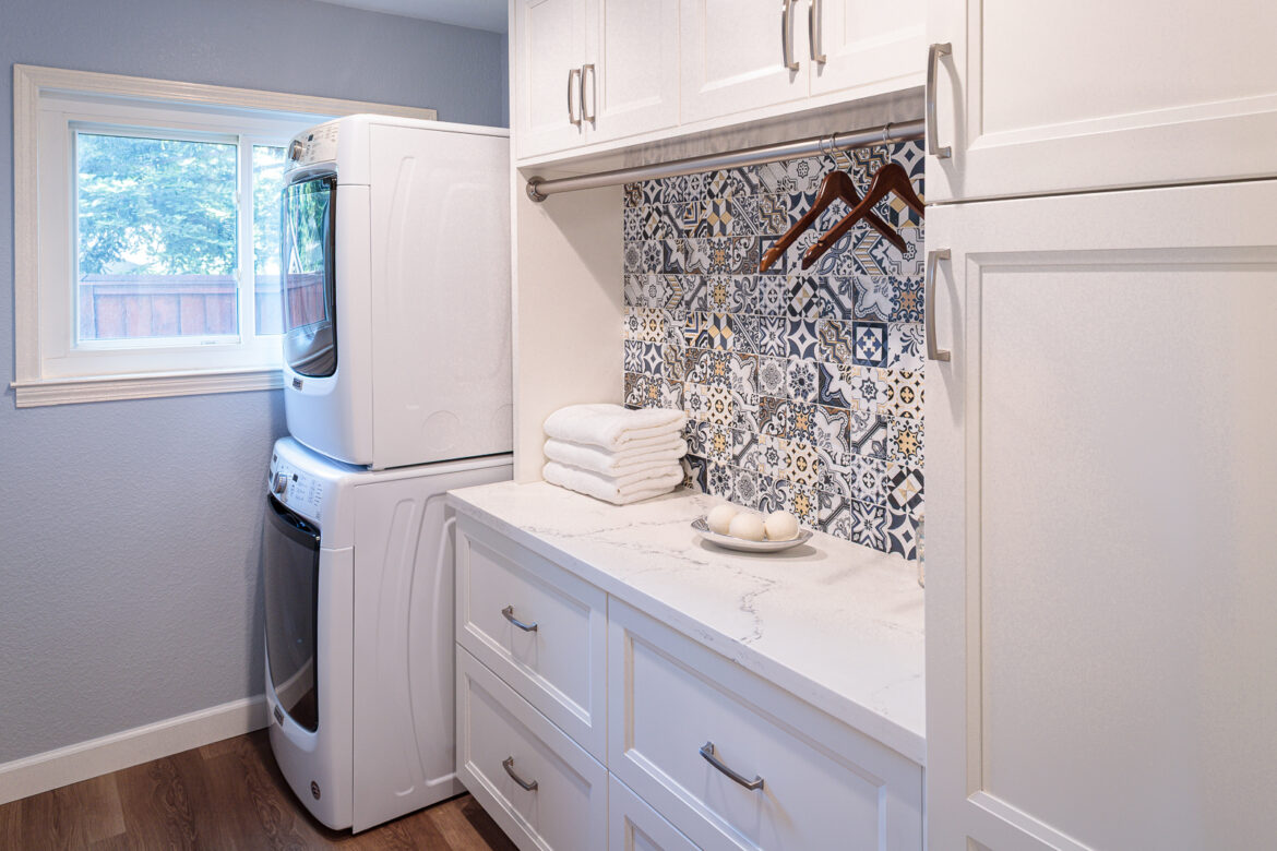 custom laundry room with blue and white tile backsplash, drying rod, quartz countertop and and stacked washer and dryer